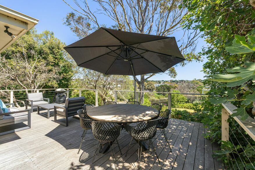 An outdoor dining setup on a sunny patio features a table surrounded by chairs and shaded by a large patio umbrella.