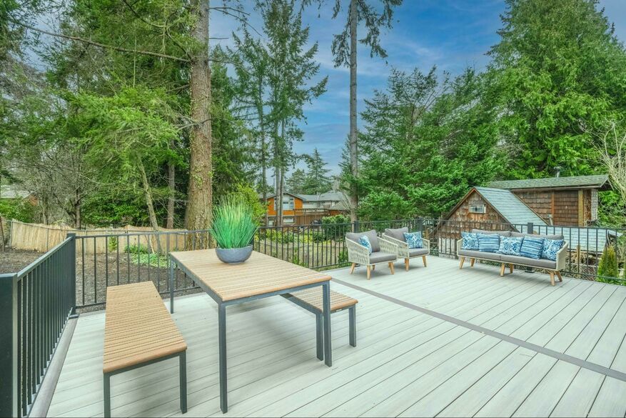 A modern deck with a table and chairs looks out onto a tree-filled backyard.