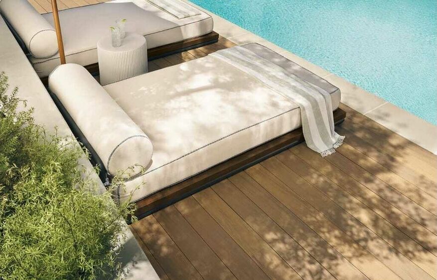 A light-colored TimberTech deck surrounds a swimming pool. White lounge chairs are located on the deck.