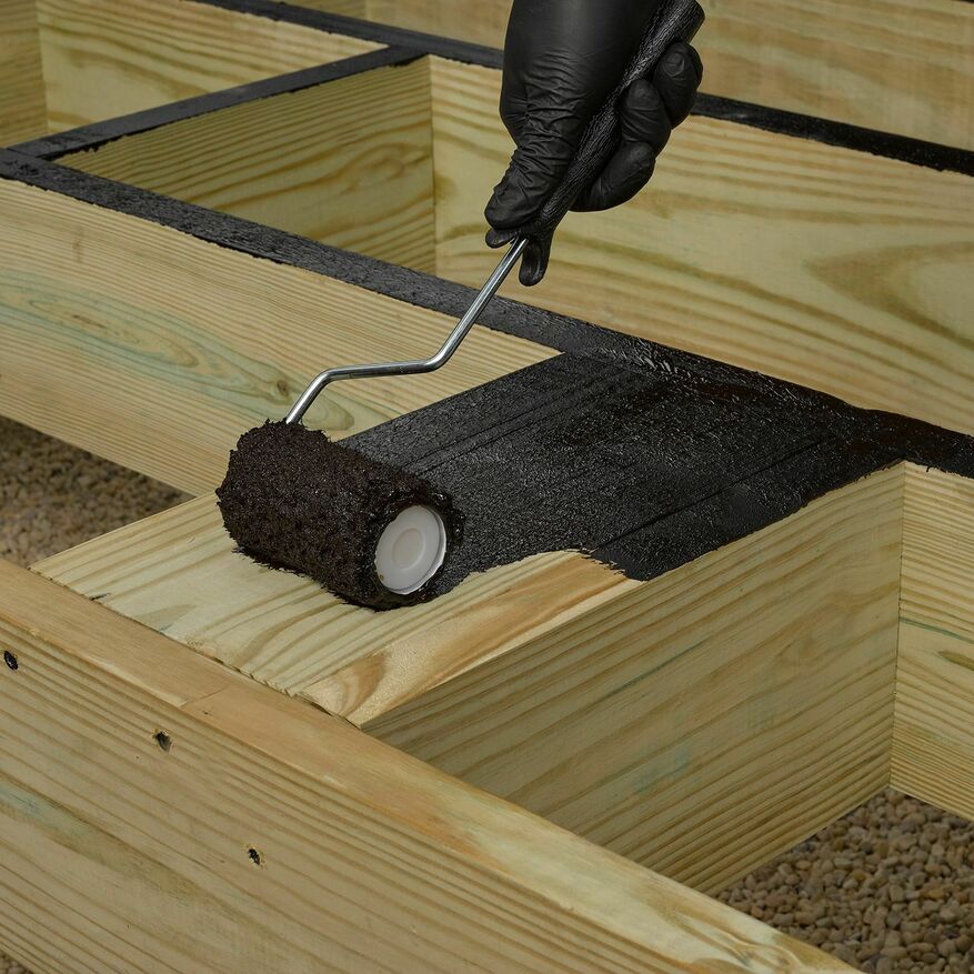 A black deck coating is applied by a roller to a wooden deck.