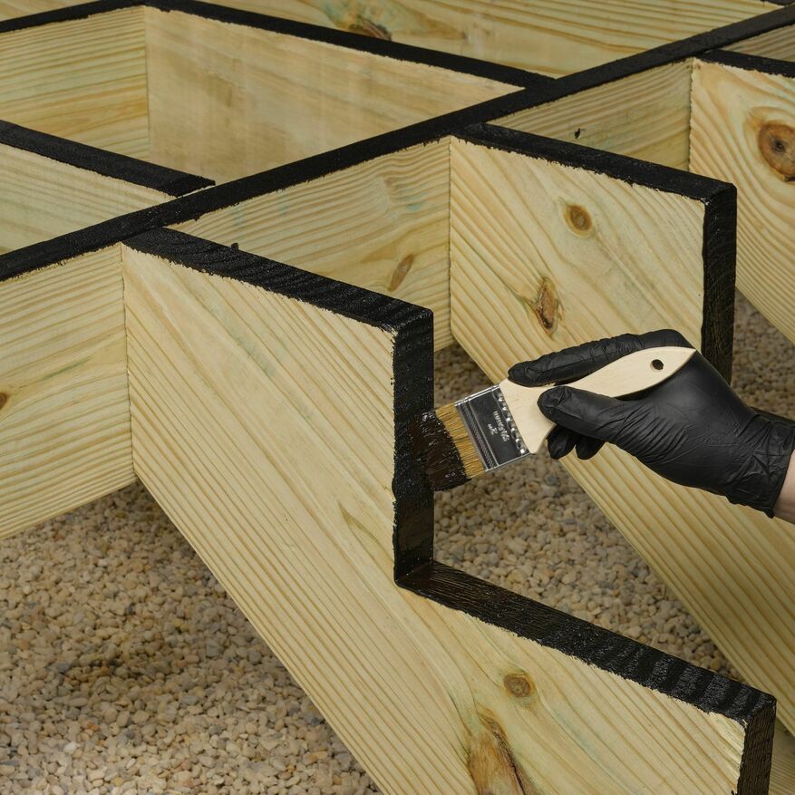 A black deck coating is applied by a brush to a wooden deck.